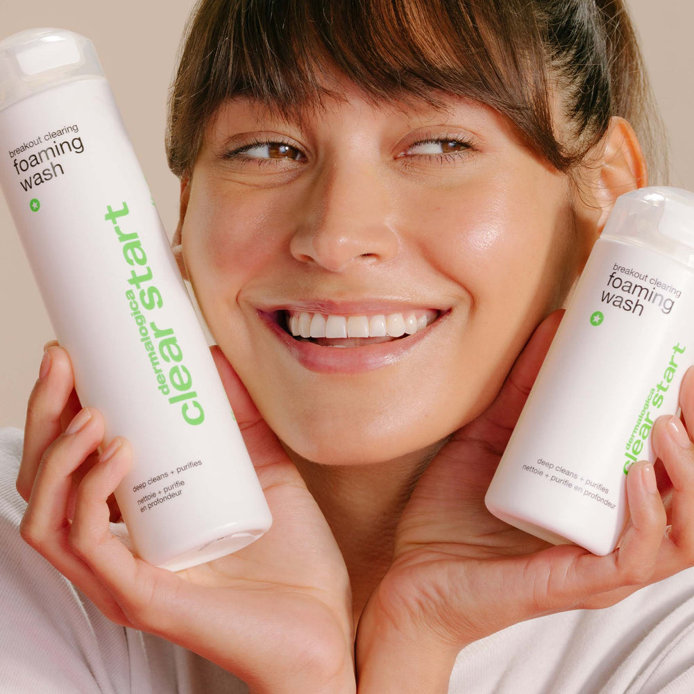 Woman holding two bottles of 'Clear Start' foaming wash with a neutral background