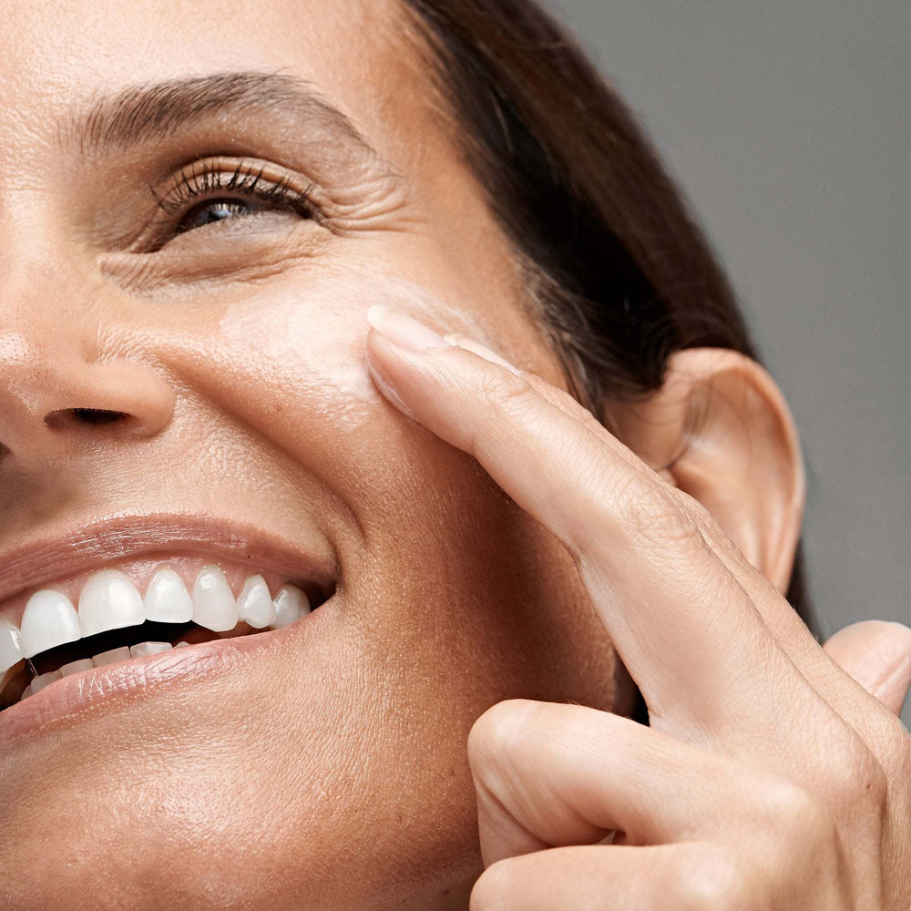 Woman applying powerbright dark spot serum to her face with a neutral background