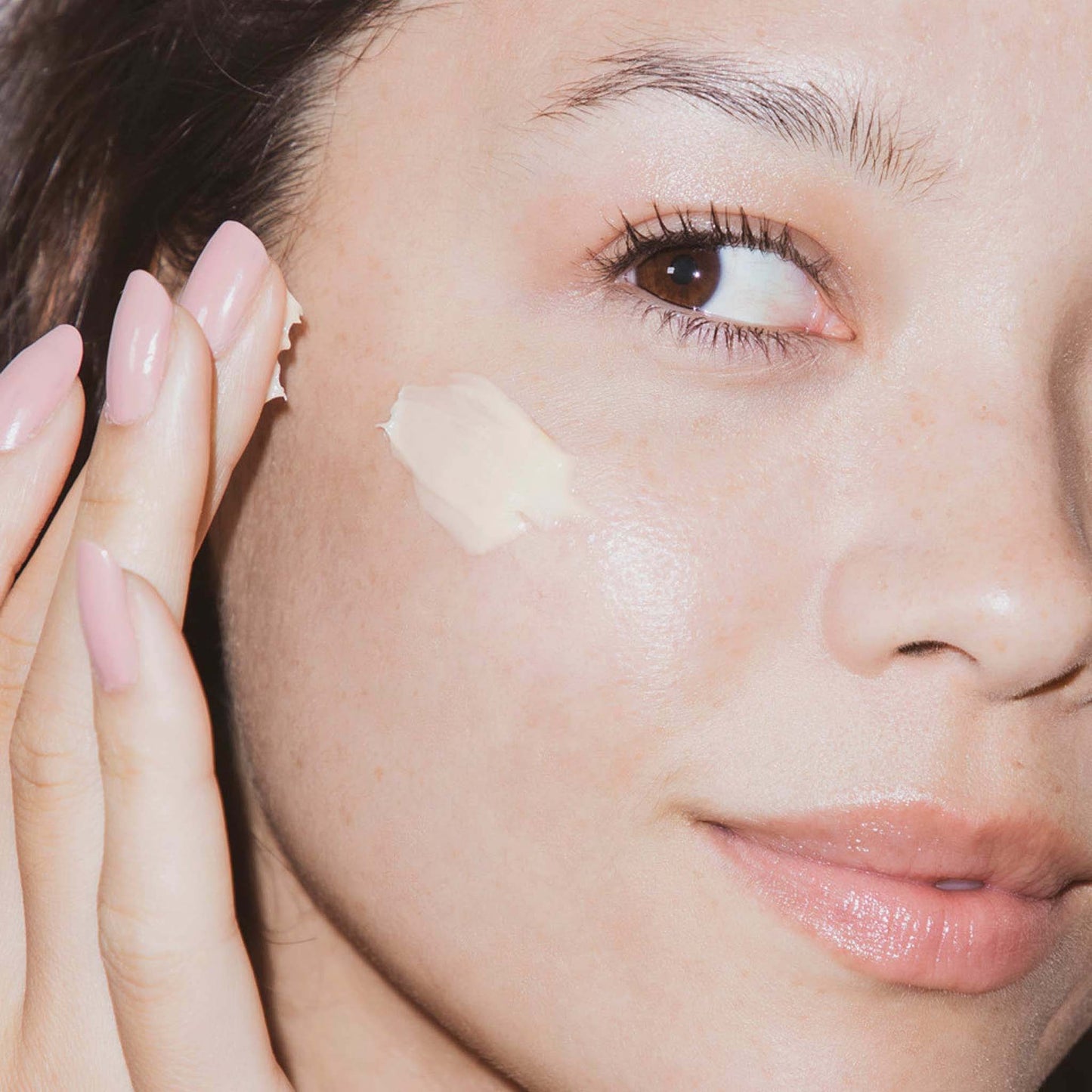 Close-up of a woman applying multivitamin power recovery masque to her face with a neutral background