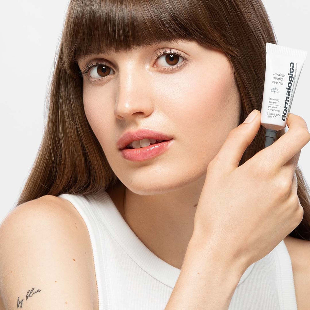 Woman holding a dermalogica awaken peptide eye gel close to her face on a white background
