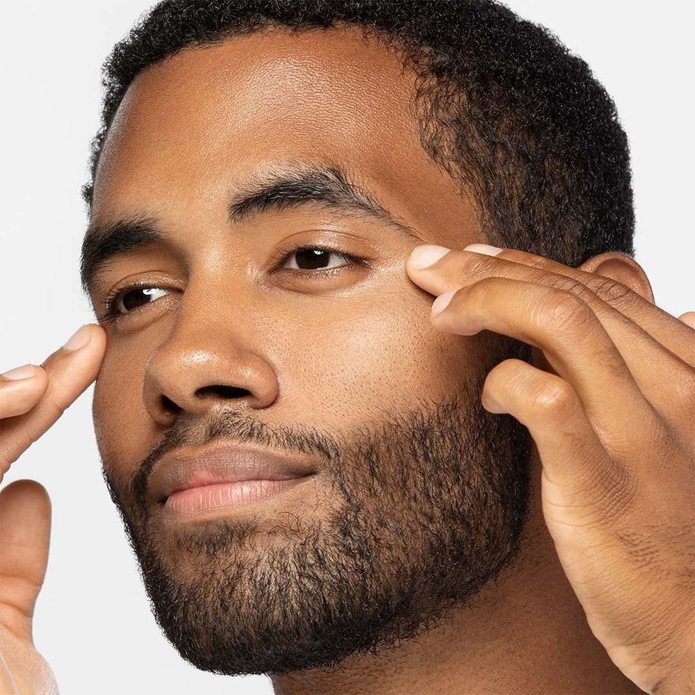 Man applying dermalogica awaken peptide eye gel to his face with a neutral background