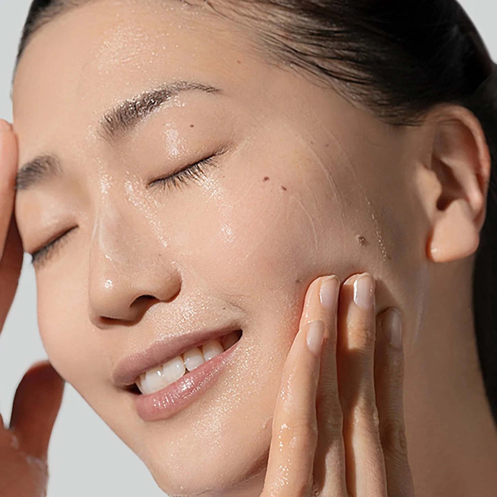 Close-up of a person applying dermalogica daily glycolic cleanser to their face with a neutral background
