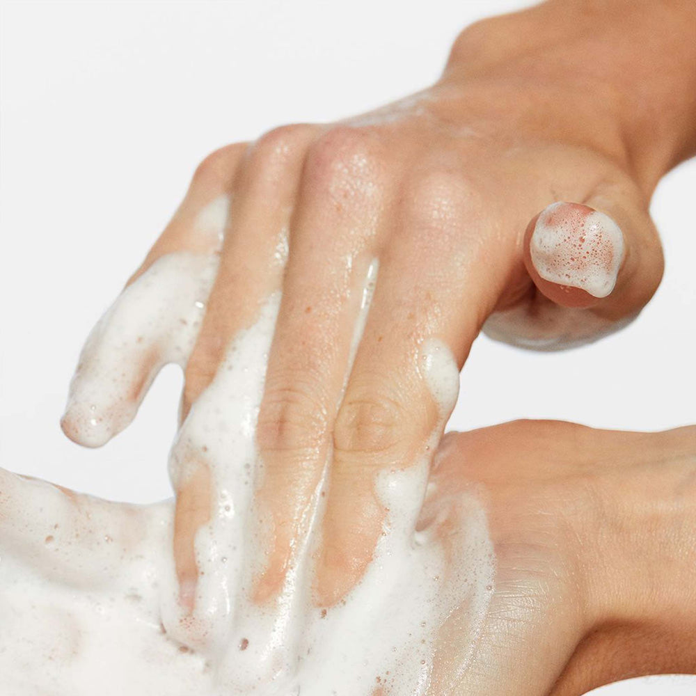 Close-up of hands with dermalogica oil to foam total cleanser suds on a light background
