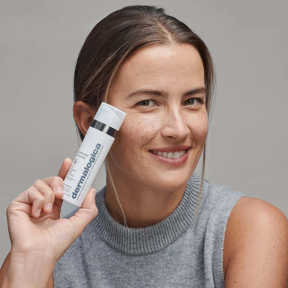 Woman holding a powerbright moisturizer against a neutral background